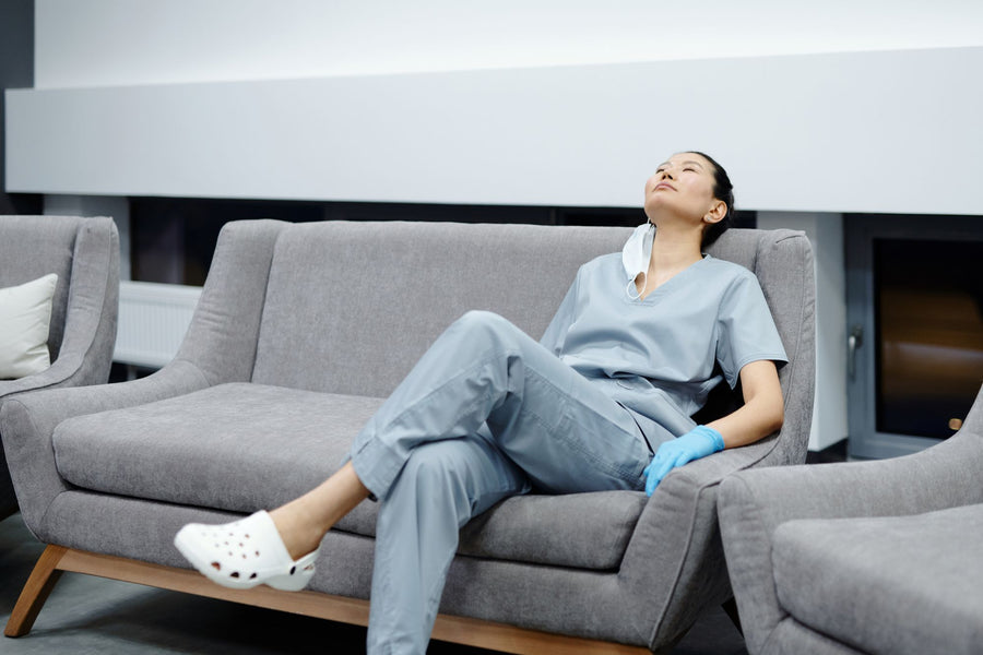 Nurse in scrubs resting on a sofa after a long shift