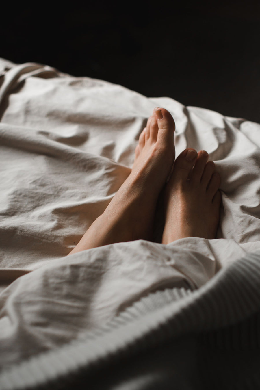 Relaxed bare feet tucked into soft bed sheets